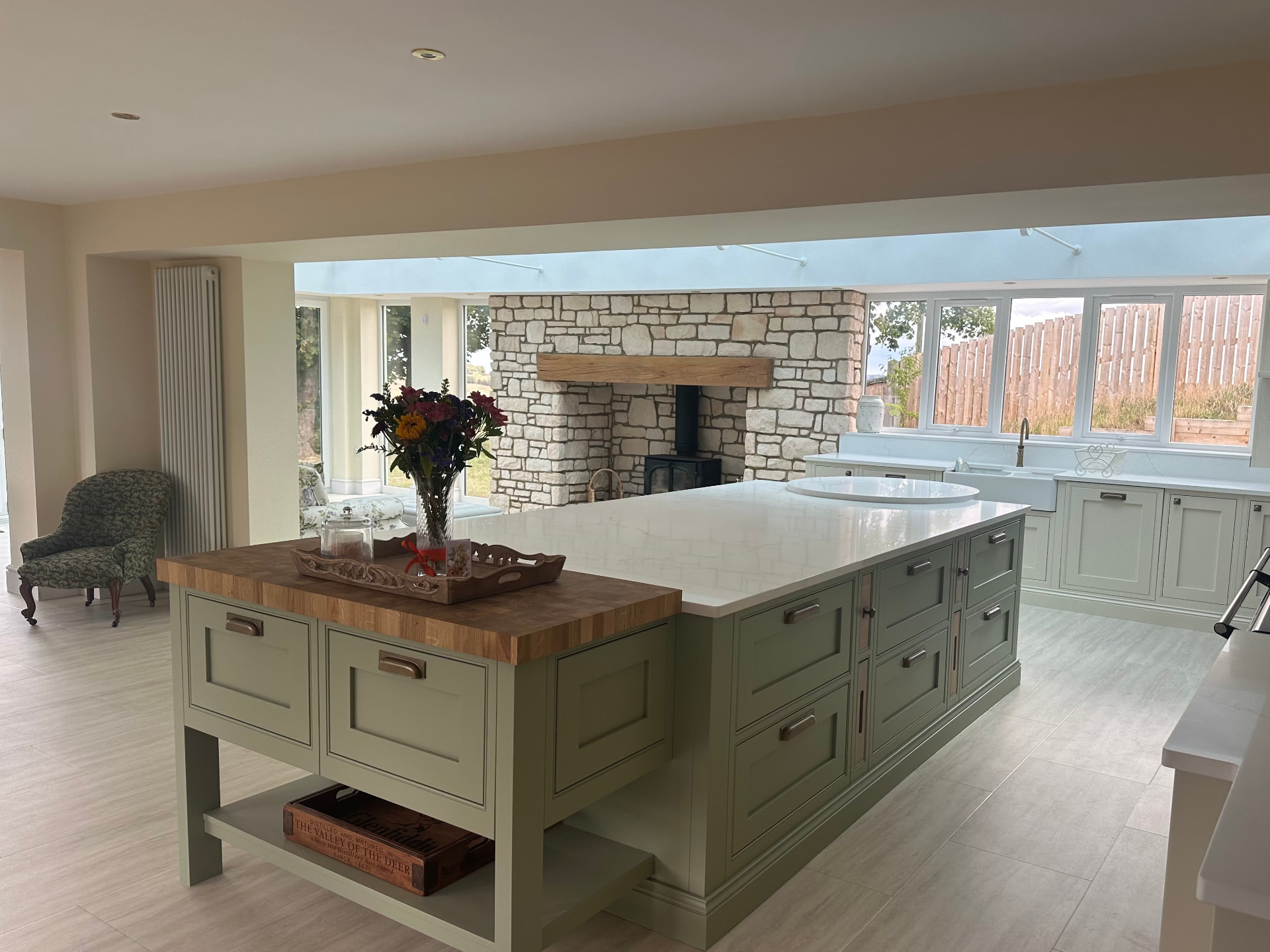 Bespoke sage green island with oak butcher block top and stone fireplace beyond