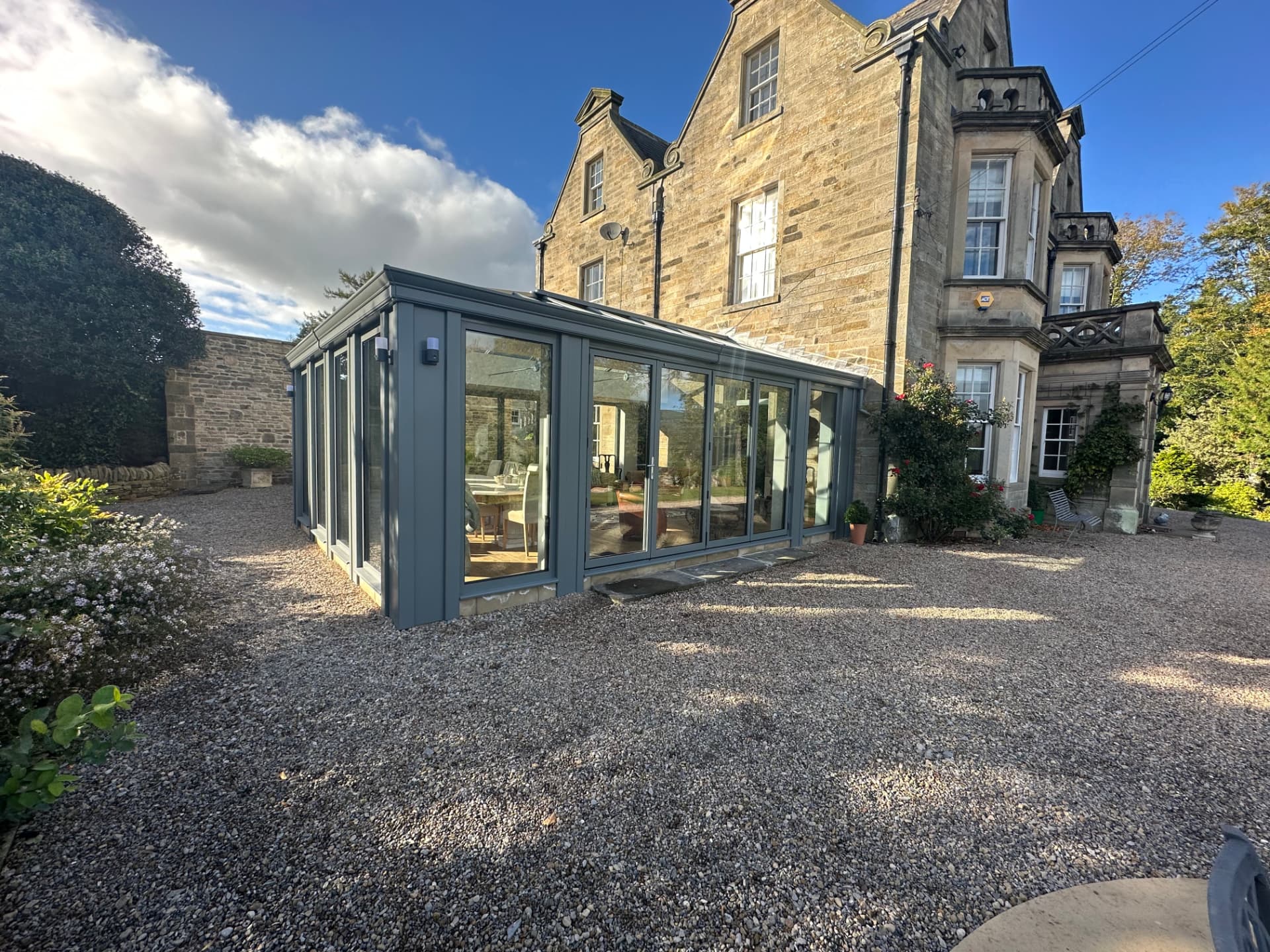Aluminium orangery with bi-folding doors closed, viewed from the gravel driveway