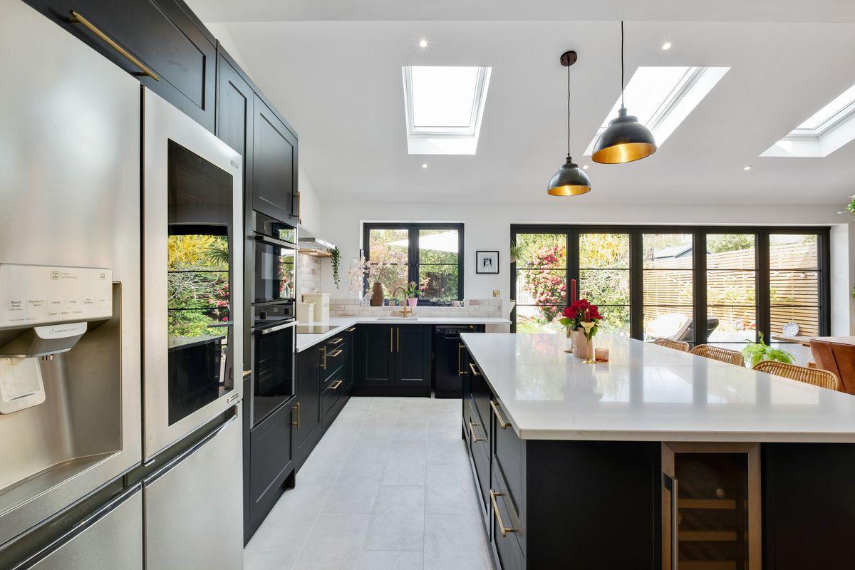 Charcoal kitchen cabinetry with brass handles and roof lights above