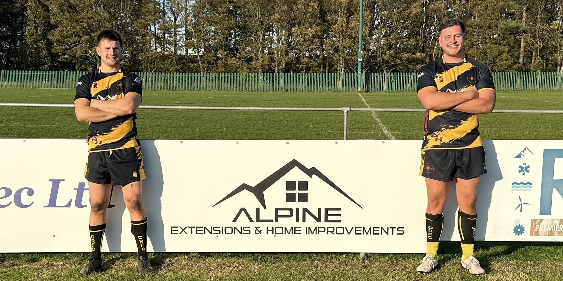 Consett Rugby Club players beside the Alpine Extensions & Home Improvements pitch-side sponsorship board
